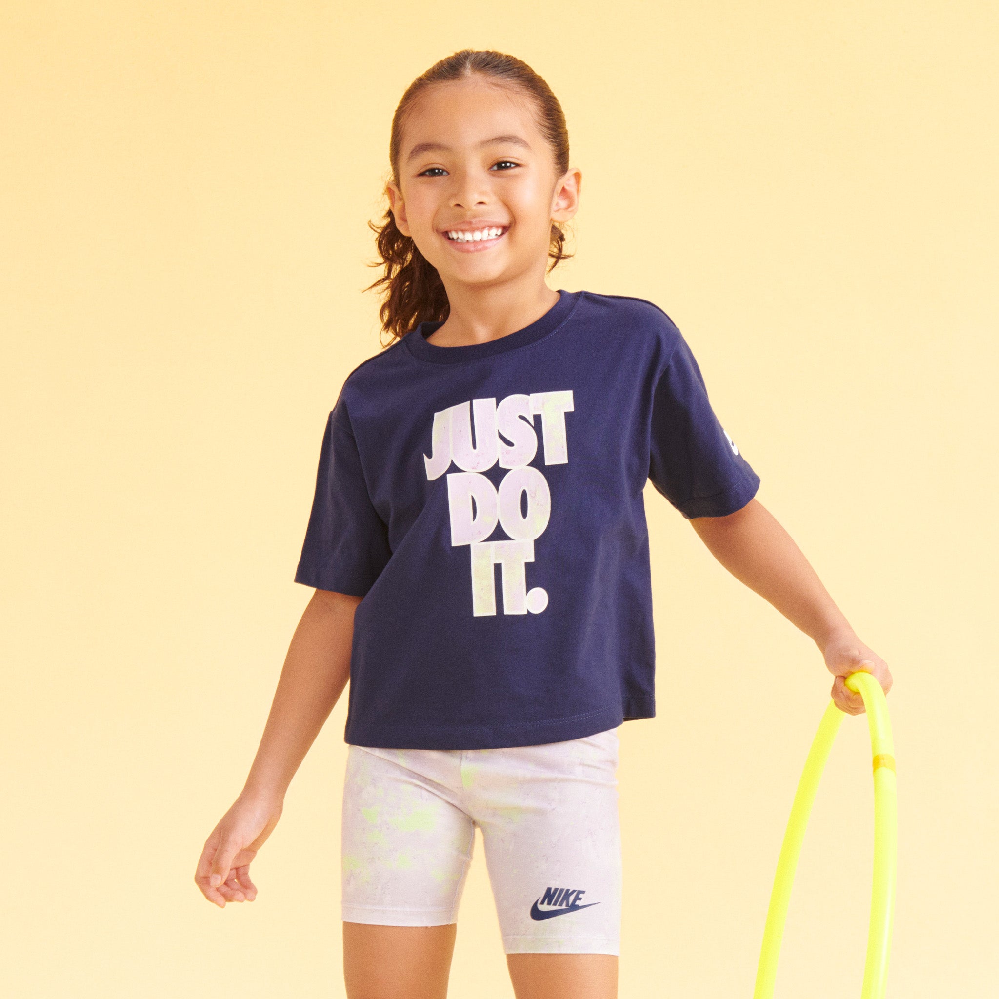 young girl wearing a navy blue Nike Just Do It t-shirt and multi-colored shorts.